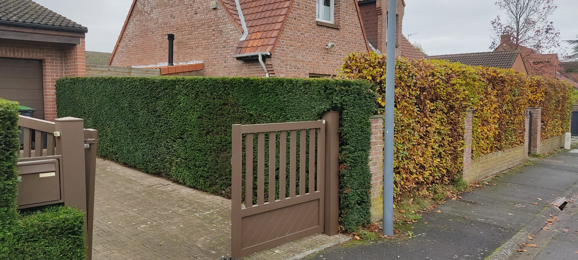 Portail en métal marron posé par un paysagiste à Lille devant une maison en briques avec haies taillées