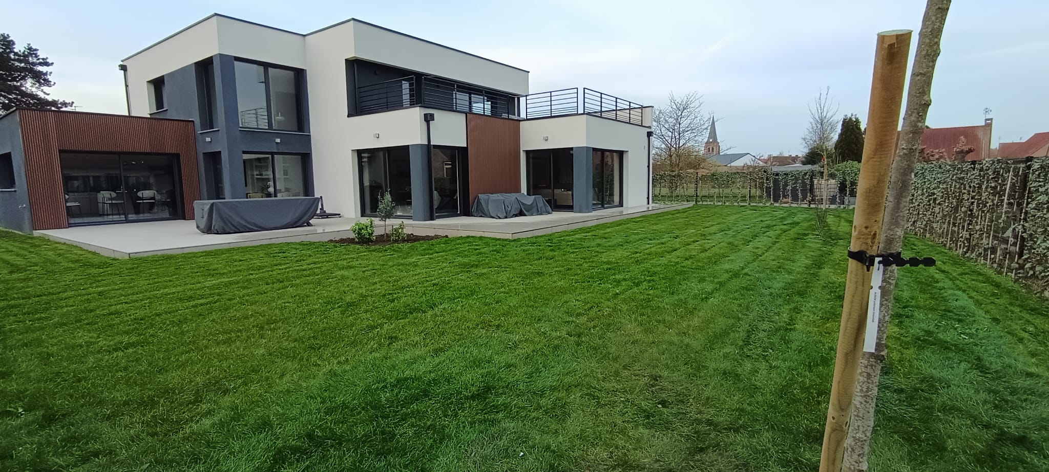 Réalisations paysagiste Lille : maison moderne avec terrasse et pelouse verte bien entretenue