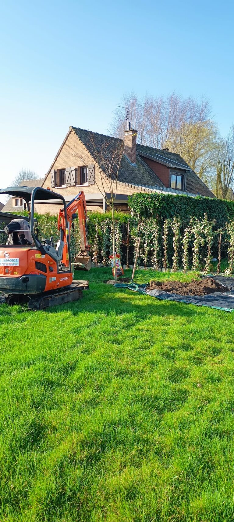 Réalisation paysagiste Lille : mini pelle creusant une pelouse devant une maison en briques