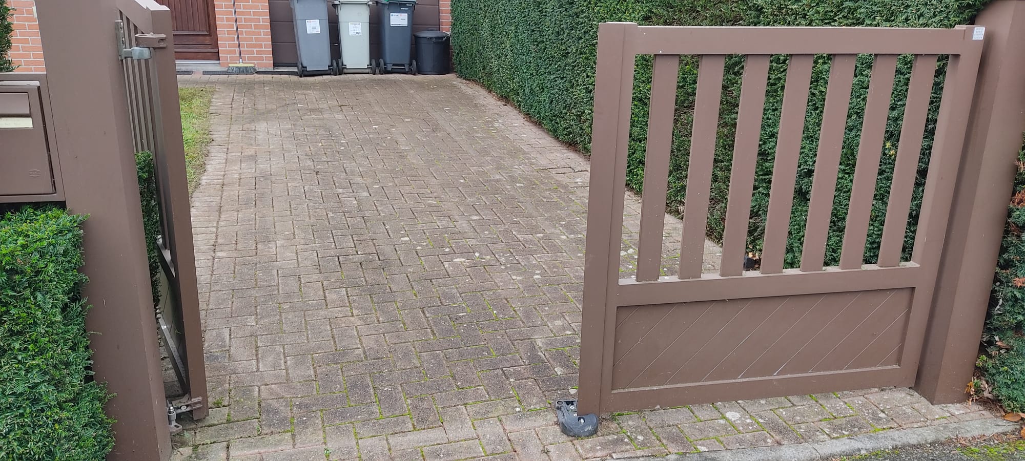 Portail en métal brun posé par un paysagiste à Lille sur une allée pavée bordée de haie
